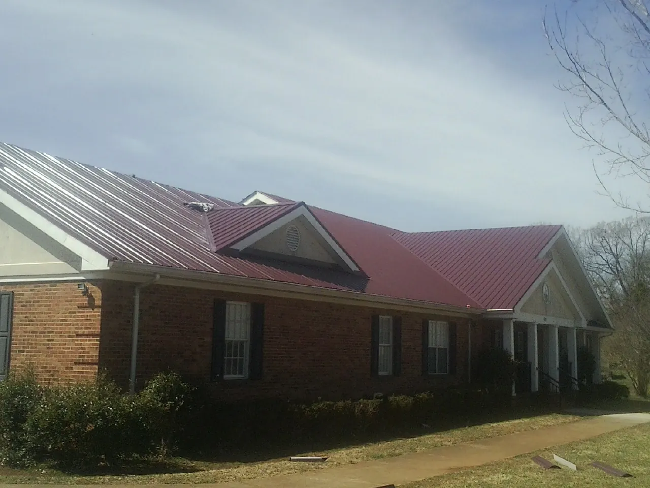 Red metal roof with gabled entries on a long brick building, from a Hail Damage Roof Repair job in Cocoa Beach