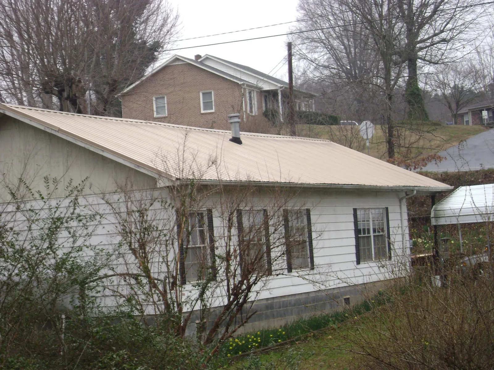 Tan metal roof on a white sided house set into a hillside — Commercial Roofing by Roofing Brothers in Cocoa Beach