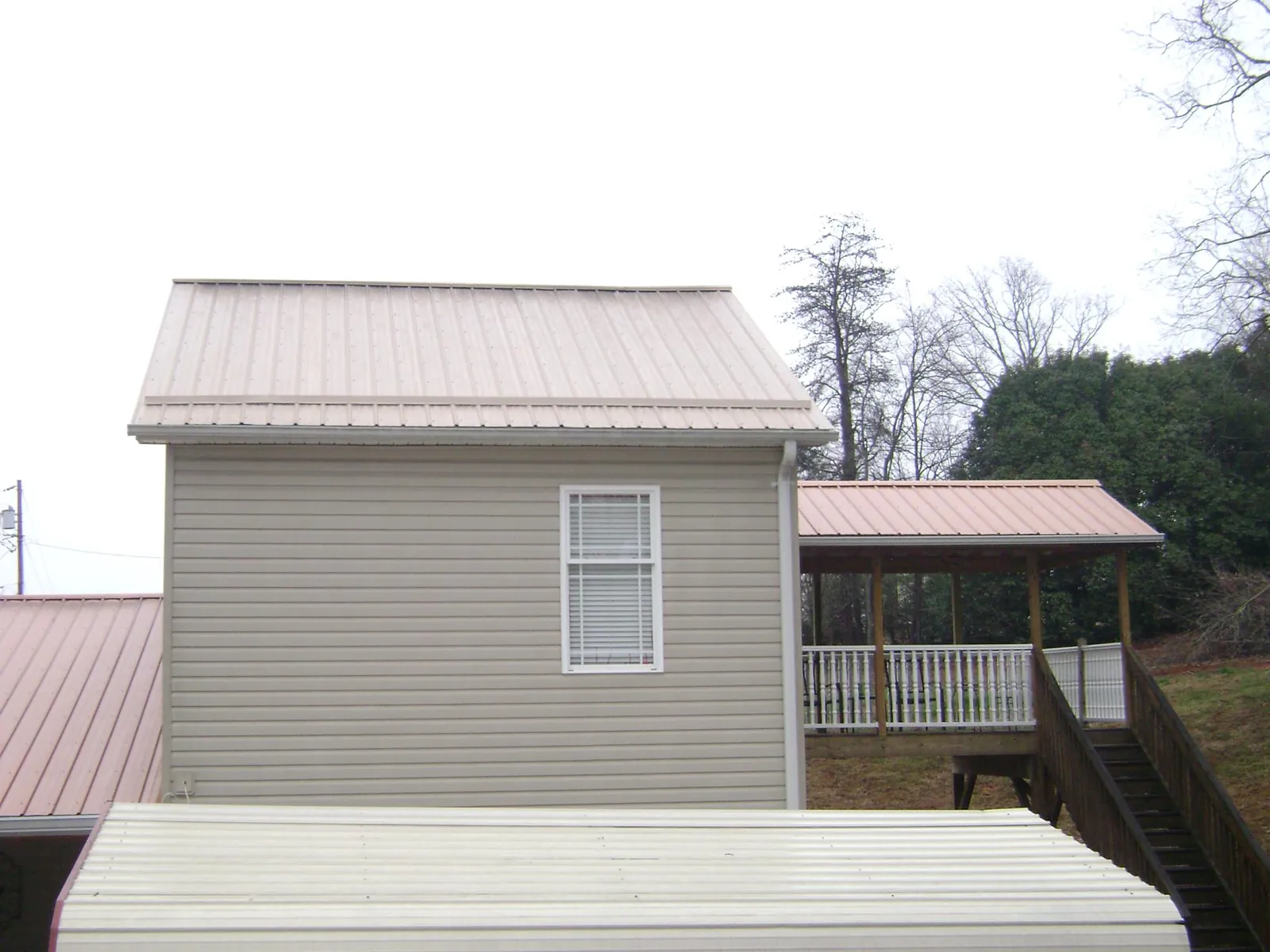 Tan metal roofs on a two story addition and attached porch, from a Roof Replacement job in Cocoa Beach
